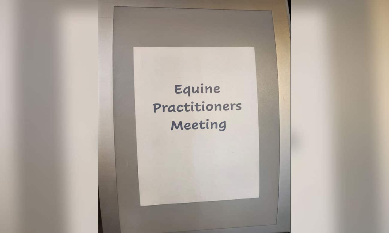 A sign on a wall reads "Equine Practitioners Meeting" in large, simple text on a white sheet of paper.